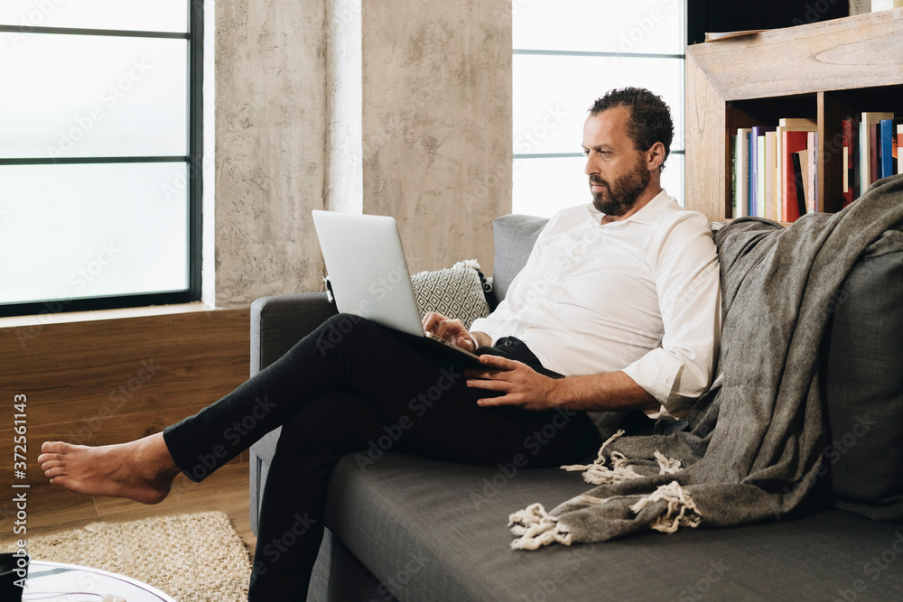 Mature man sitting on couch, using laptop Mature man sitting on couch, using laptop