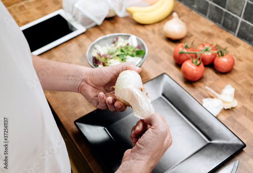 Mature man standing in kitchen, peeling onions