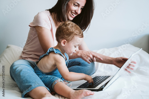 Mother and baby girl using laptop on bed at home