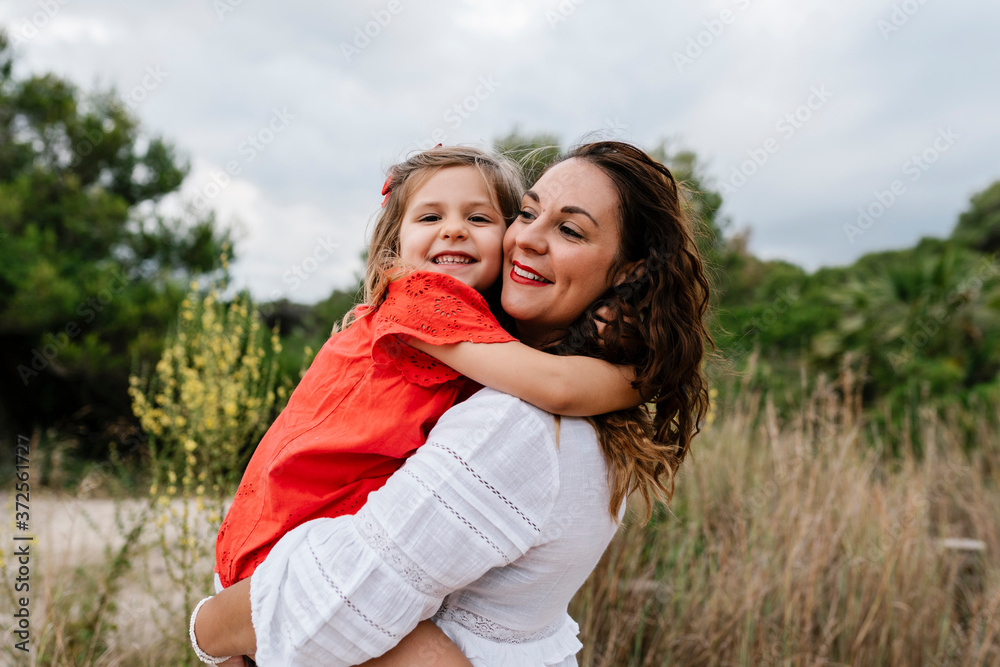 Happy woman carrying daughter at countryside against cloudy sky Happy woman carrying daughter at countryside against cloudy sky