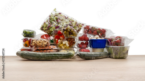 In Plastik verpackte Lebensmittel auf einer Holzplatte mit weißem Hintergrund.