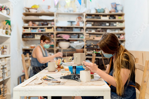 Women wearing masks making ceramics on bench in workshop photo