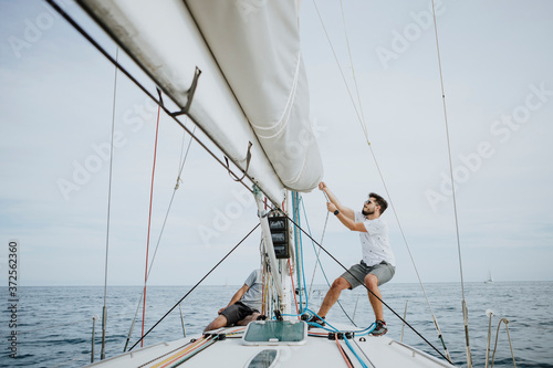 Sailor maneuvering setting the mainsail in sailboat against sky