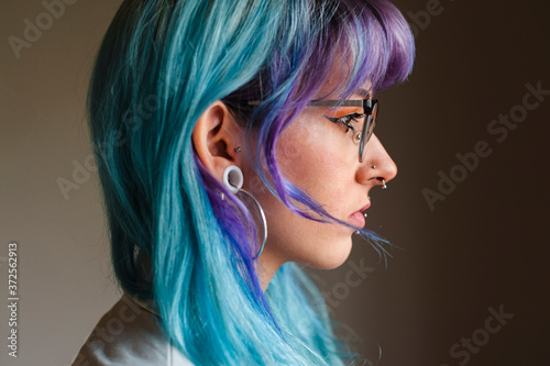Close-up of thoughtful young woman with dyed hair and piercings against wall in old office