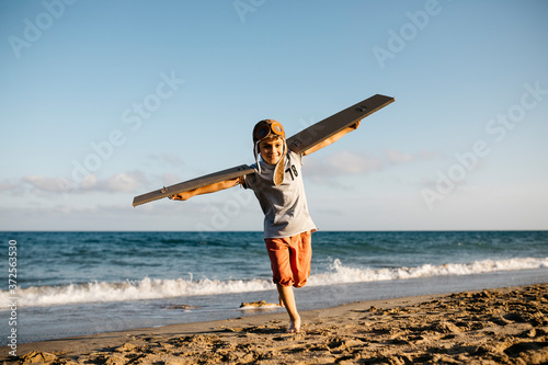 Boy running with cardboard wings and aviator's cap at beach photo