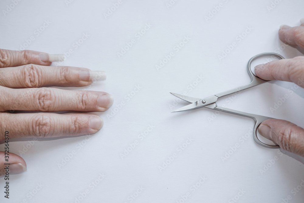 Female hand with nails of different lengths with long and short nails on the left and manicure scissors on the right, fingernail cutting/trimming and manicure. Female hand with nails of different lengths with long and short nails on the left and manicure scissors on the right, fingernail cutting/trimming and manicure.
