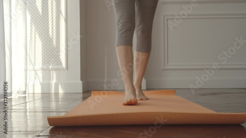 Young sport woman opens a mat getting started yoga at home