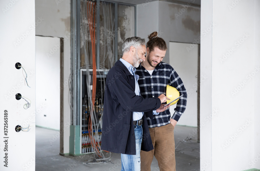 Architect and construction worker discussing over digital tablet while standing in renovating house