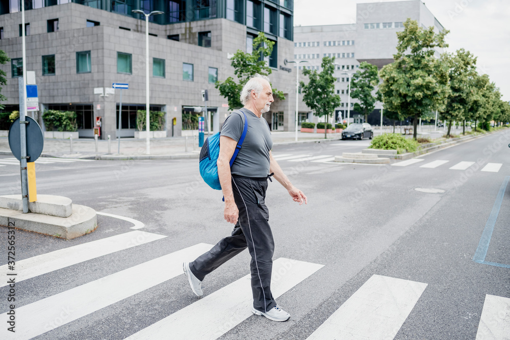 Senior man with backpack crossing road in city Senior man with backpack crossing road in city