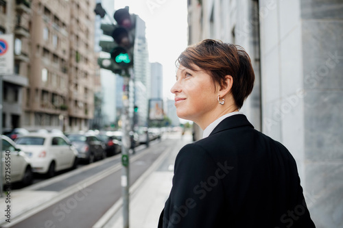 Smiling businesswoman looking away while standing against building in city photo