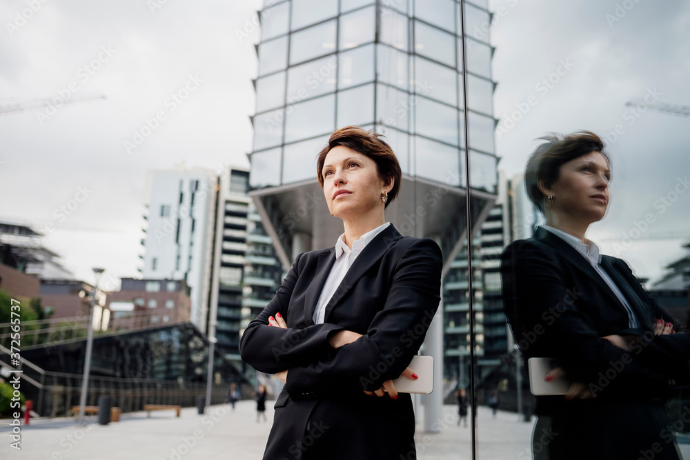 Thoughtful businesswoman with arms crossed standing by modern building in city Thoughtful businesswoman with arms crossed standing by modern building in city