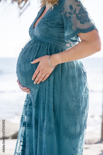 Close up of pregnant woman in a teal dress holding her belly by the ocean