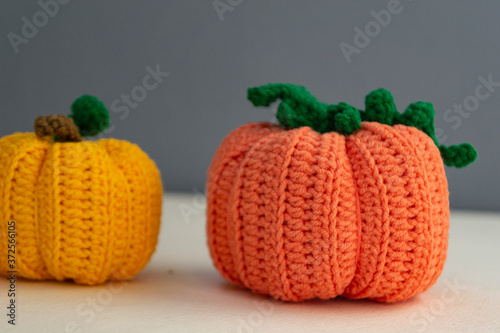 Autumn composition of two pumpkins, knitted pumpkin decor of orange and yellow on a gray background, yarn and needlework, soft light
