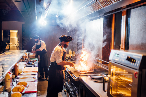 Chefs wearing protective face masks preparing a dish in restaurant kitchen photo