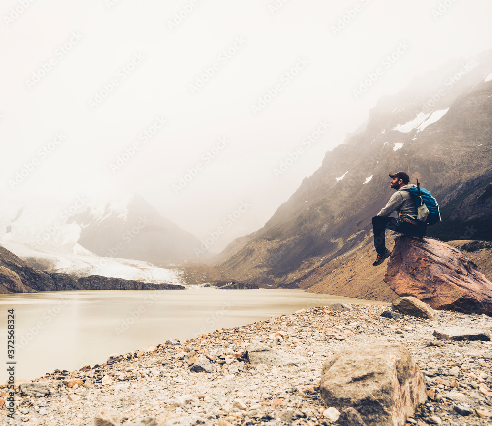 Mature man with backpack looking at lake while sitting on rock, Patagonia, Argentina Mature man with backpack looking at lake while sitting on rock, Patagonia, Argentina