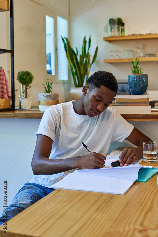Young man writing notes in book on table while sitting at home Young man writing notes in book on table while sitting at home