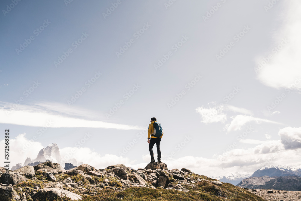 Hiker with backpack standing on mountain against sky during sunny day, Patagonia, Argentina Hiker with backpack standing on mountain against sky during sunny day, Patagonia, Argentina