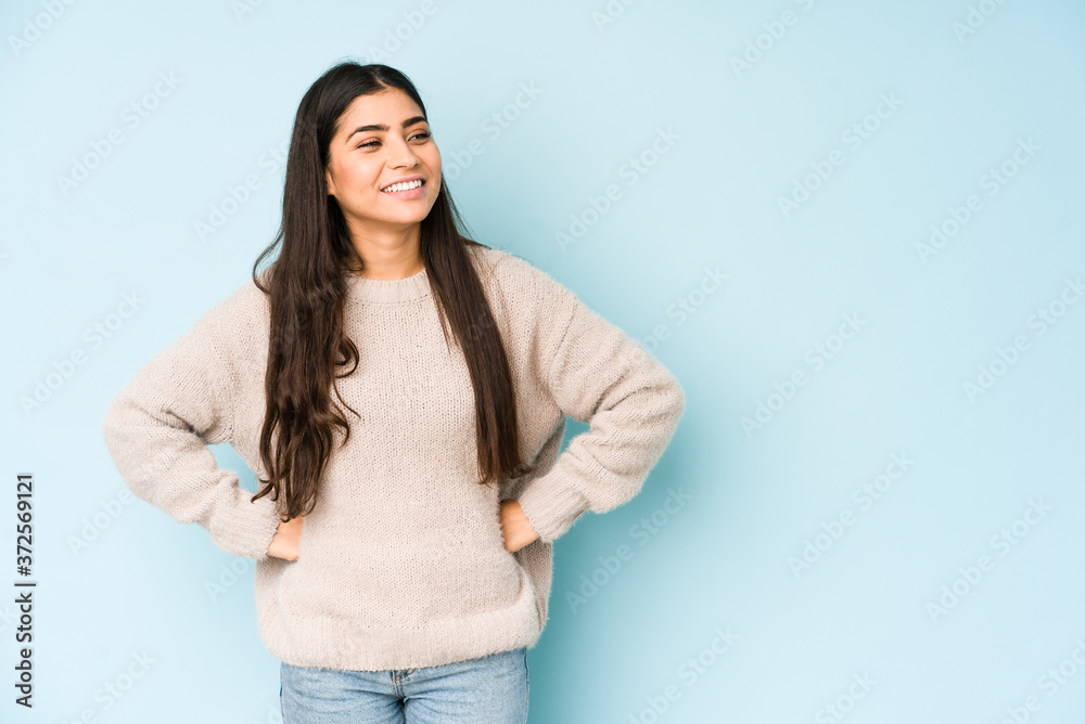 Young indian woman isolated on blue background confident keeping hands on hips. Young indian woman isolated on blue background confident keeping hands on hips.