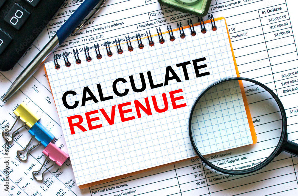 Text Calculate Revenue on notepad with calculator, clips, pen on financial report Text Calculate Revenue on notepad with calculator, clips, pen on financial report