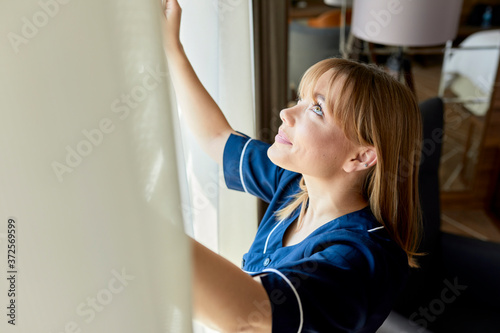 Close-up of chambermaid opening curtains of window in hotel room