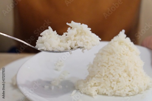 In selective focus a man hand holding a spoon of Jasmine rice with blurred a white dish on a dinning table 