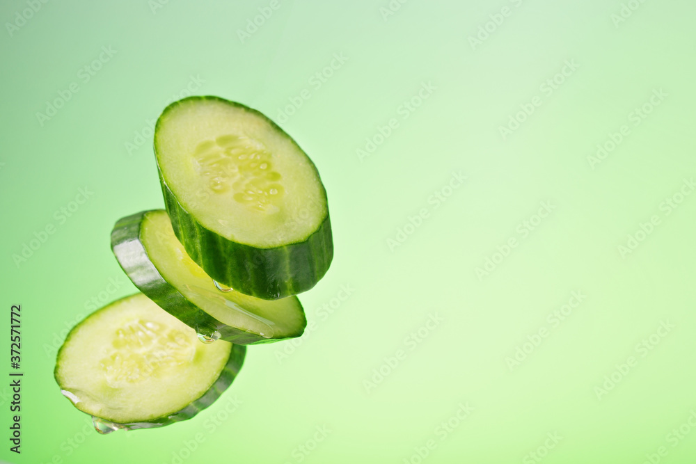 Pieces of cucumber in free fall with drops of oil on a green background with a gradient