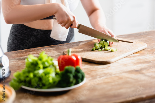 cropped view of young woman cutting cucumber on chopping board
