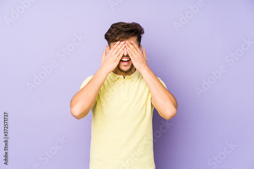 Young arabian man isolated on a purple background covers eyes with hands, smiles broadly waiting for a surprise.