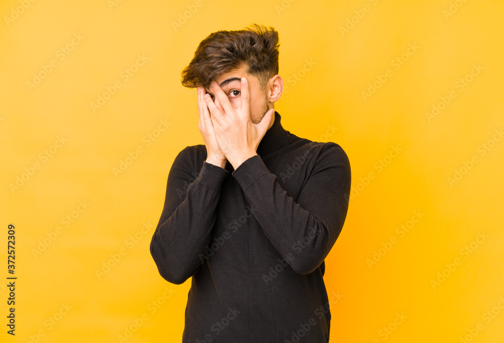 Young arabian man isolated on a yellow background blink through fingers frightened and nervous. Young arabian man isolated on a yellow background blink through fingers frightened and nervous.