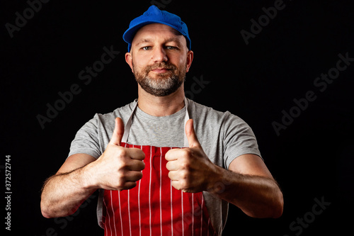 Slika na platnu Professional butcher fishmonger in grey t shirt and classic red and white stripe apron and blue baseball hat