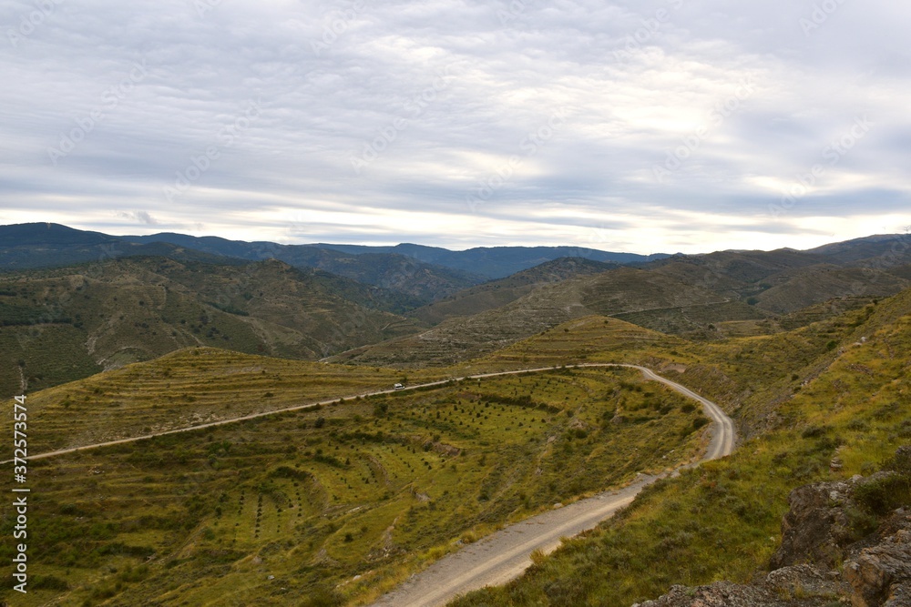 Naklejka premium Mountain landscape with forest track and van going up. Cloudy sky at sunset.