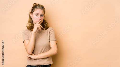 Young caucasian woman isolated on beige background looking sideways with doubtful and skeptical expression.