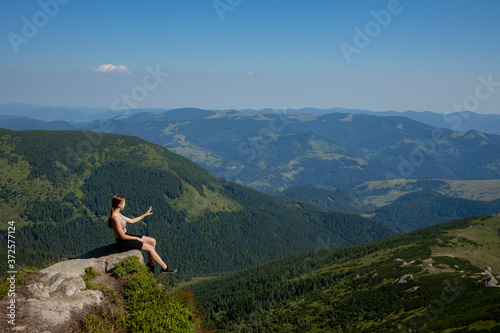 A girl sits on the edge of the cliff and looking at the sun valley and mountains © volody10