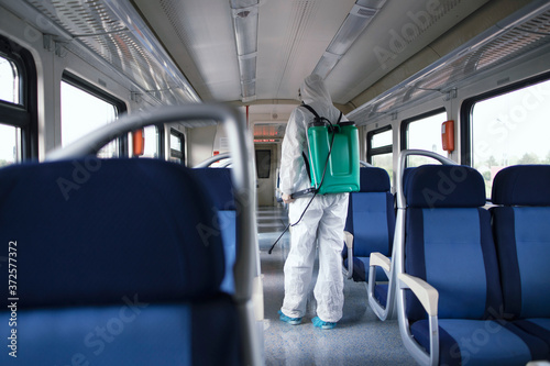 Public transportation healthcare. Man in white protection suit disinfecting and sanitizing subway train interior to stop spreading highly contagious coronavirus or COVID-19.