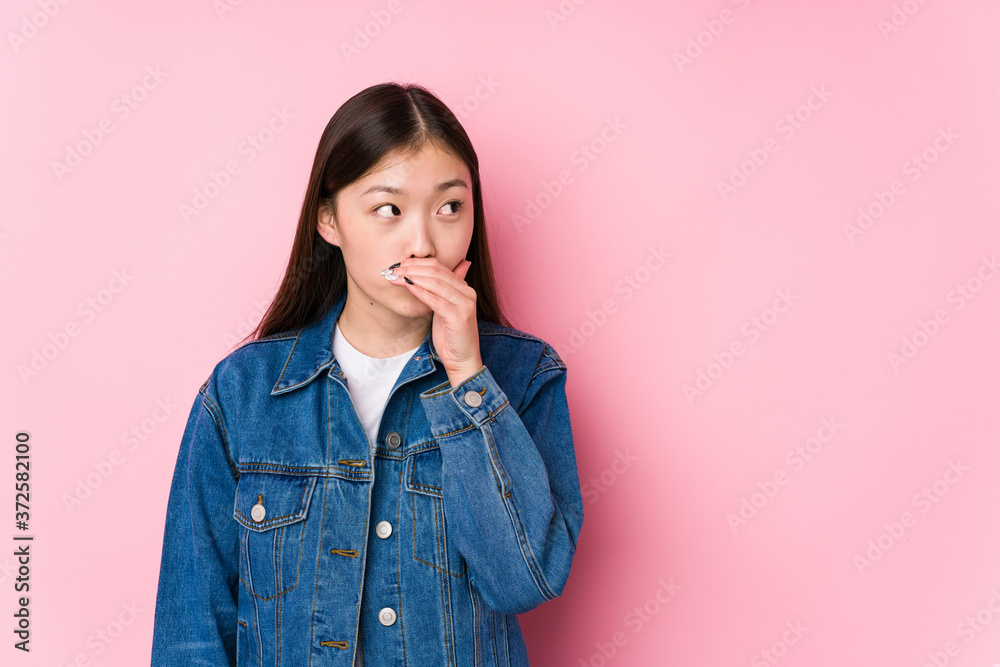 Young chinese woman posing in a pink background isolated thoughtful looking to a copy space covering mouth with hand. Young chinese woman posing in a pink background isolated thoughtful looking to a copy space covering mouth with hand.
