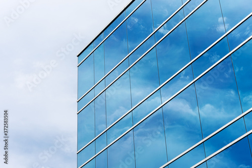 View of typical blue glass facade of generic modern office building. Beautiful clouds and blue sky reflected in the mirrored windows of a corporate office building.