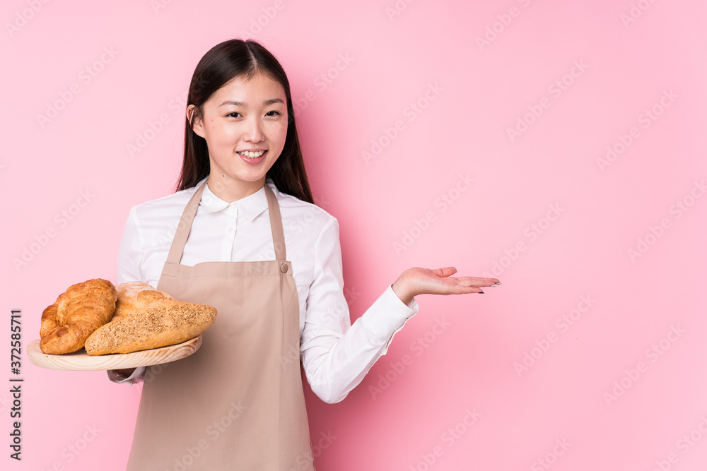 Young chinese baker woman isolated showing a copy space on a palm and holding another hand on waist. Young chinese baker woman isolated showing a copy space on a palm and holding another hand on waist.