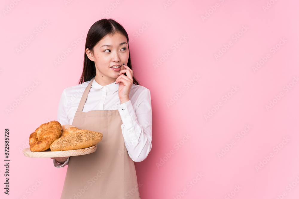 Young chinese baker woman isolated relaxed thinking about something looking at a copy space. Young chinese baker woman isolated relaxed thinking about something looking at a copy space.