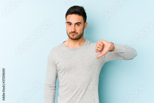 Young caucasian man isolated on blue background showing a dislike gesture, thumbs down. Disagreement concept.