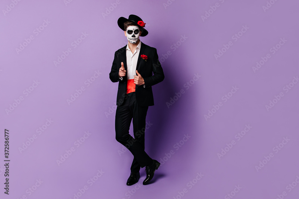 Full-length shot of charming guy with red satin belt under black jacket, posing in Halloween costume Full-length shot of charming guy with red satin belt under black jacket, posing in Halloween costume