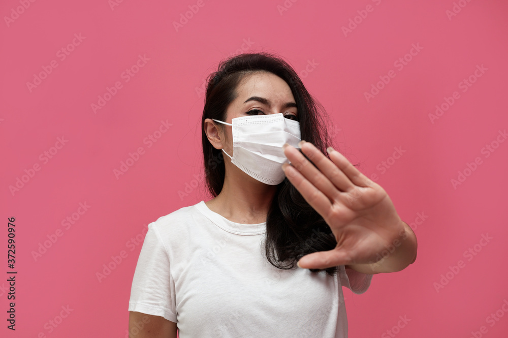 young asian woman wearing protection mask or surgical mask for protected virus and air pollution making hand stop virus on pink background,Health care and coronavirus concept young asian woman wearing protection mask or surgical mask for protected virus and air pollution making hand stop virus on pink background,Health care and coronavirus concept