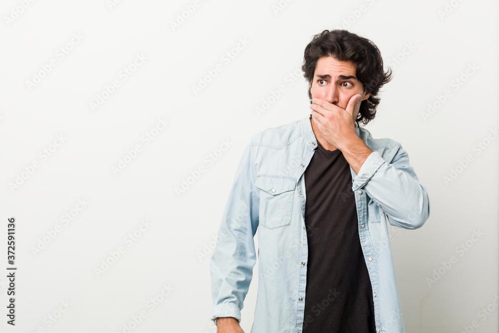 Young handsome man against a white background thoughtful looking to a copy space covering mouth with hand. Young handsome man against a white background thoughtful looking to a copy space covering mouth with hand.