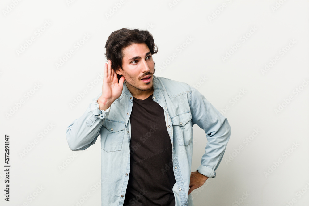 Young handsome man against a white background trying to listening a gossip. Young handsome man against a white background trying to listening a gossip.