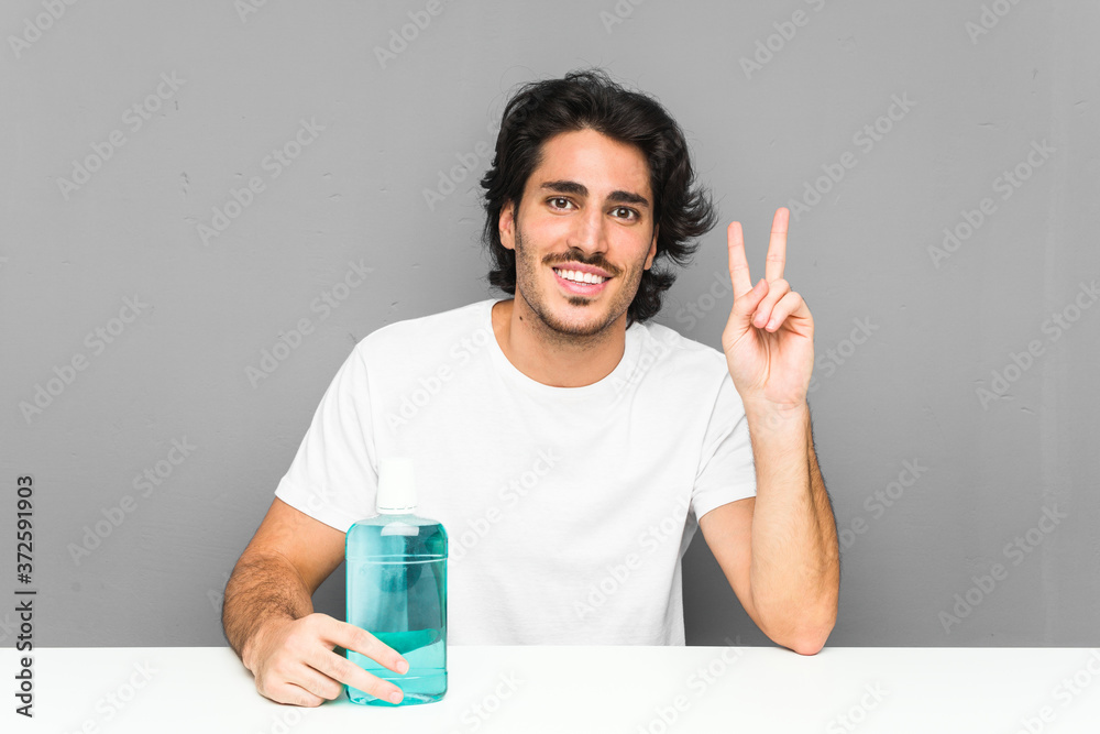Young man holding a mouthwash showing victory sign and smiling broadly. Young man holding a mouthwash showing victory sign and smiling broadly.