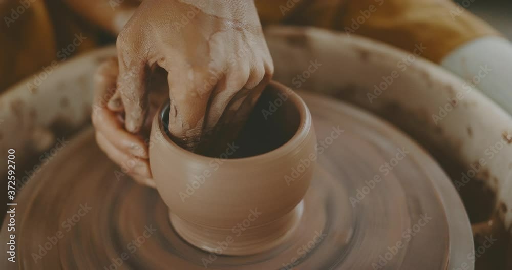Talented woman making clay bowl on pottery wheel, close up of hands and clay, handmade