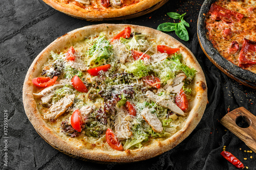 Tasty pizza with chicken meat, cheese, lettuce, sauce and tomatoes on stone black background. Fast food lunch for picnic company, top view, selective focus