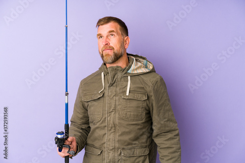 Senior fisherman isolated on purple background dreaming of achieving goals and purposes