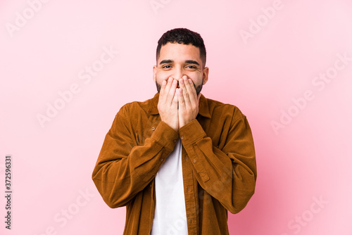 Young latin man against a pink background isolated laughing about something  covering mouth with hands.