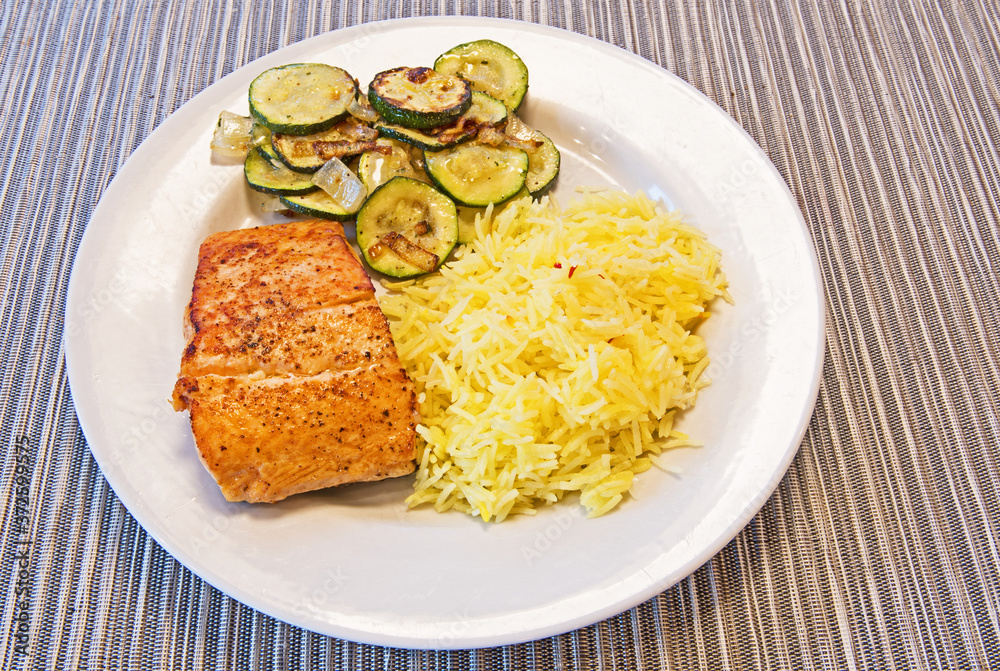 A dinner plate of fresh Atlantic salmon, saffron rice and courgettes cooked with onions.