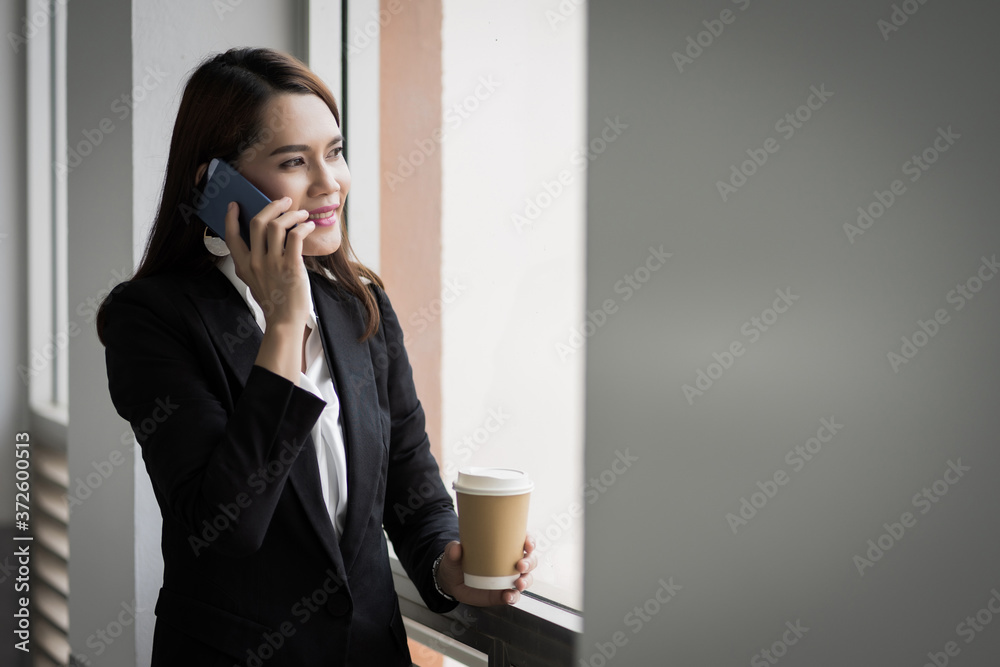 Portrait of a young Asian business woman talking over cellphone and holding cup of coffee in business building. Photo of beautiful girl in casual suite with phone and cup of coffee. Portrait of a young Asian business woman talking over cellphone and holding cup of coffee in business building. Photo of beautiful girl in casual suite with phone and cup of coffee.